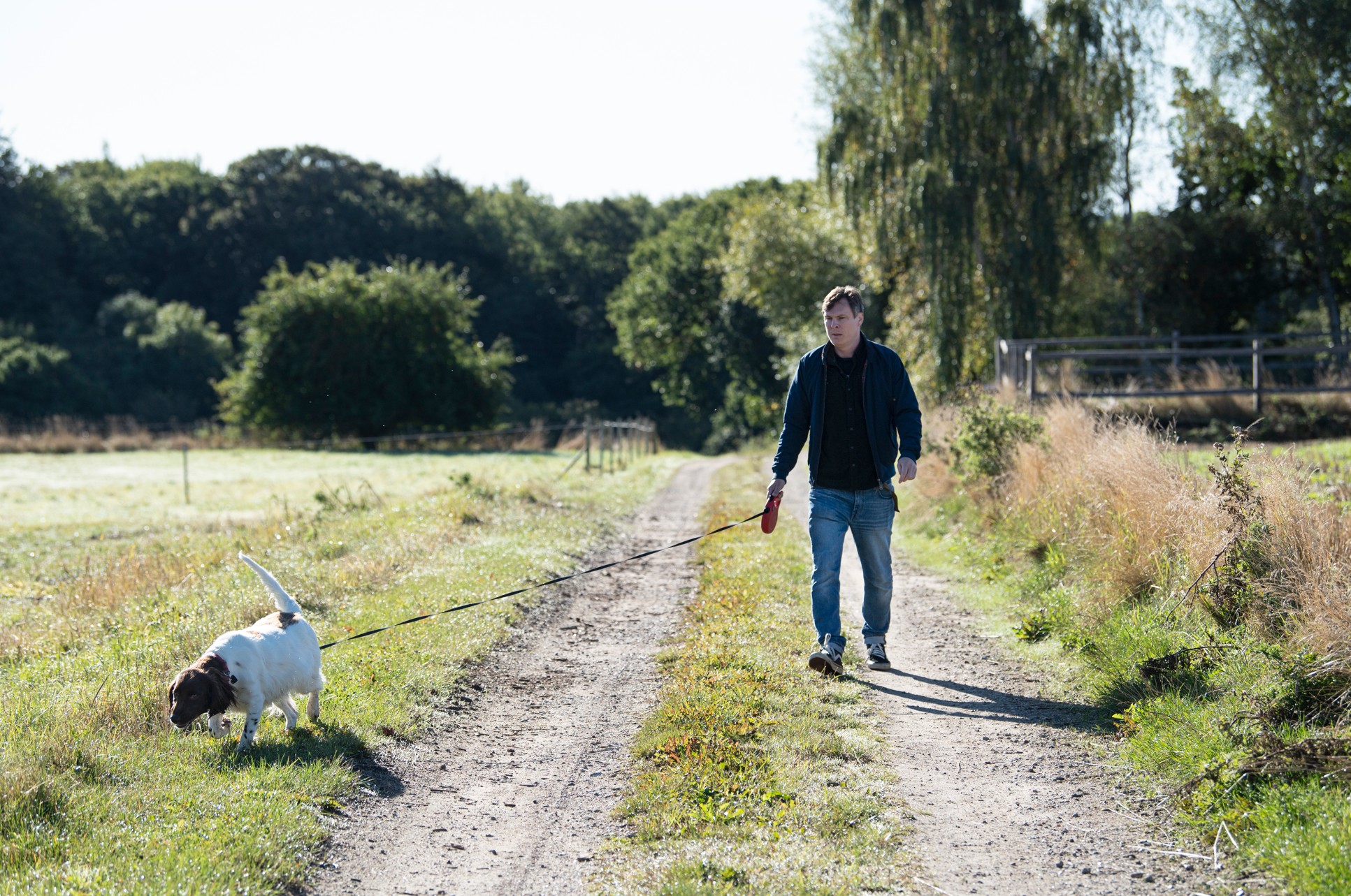 En mand går tur med hund på lang markvej