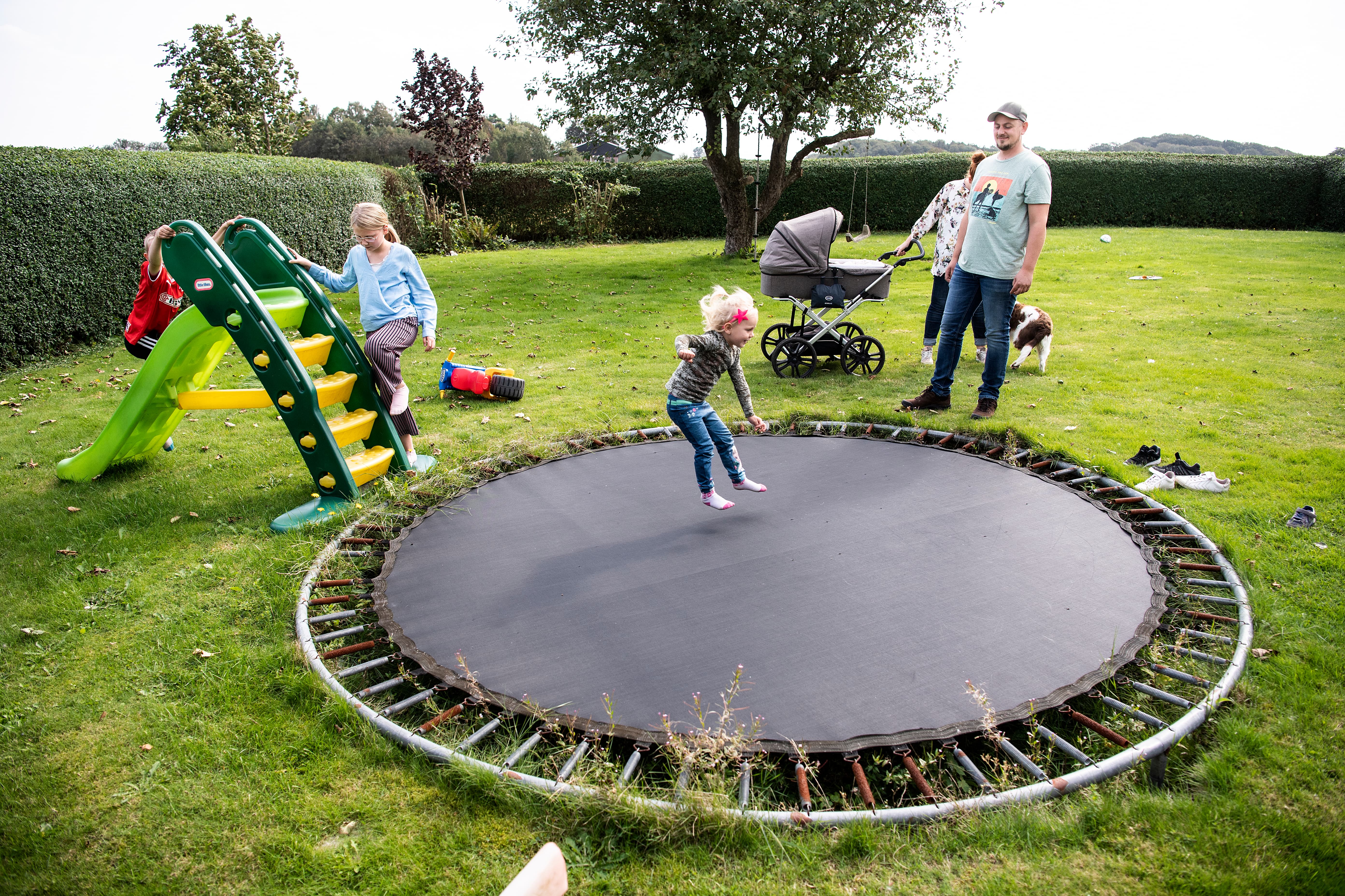Børn leger på trampolin i stor have mens mor og far kigger på