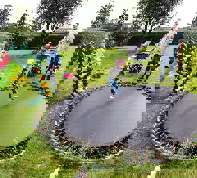 Børn leger på trampolin i stor have mens mor og far kigger på