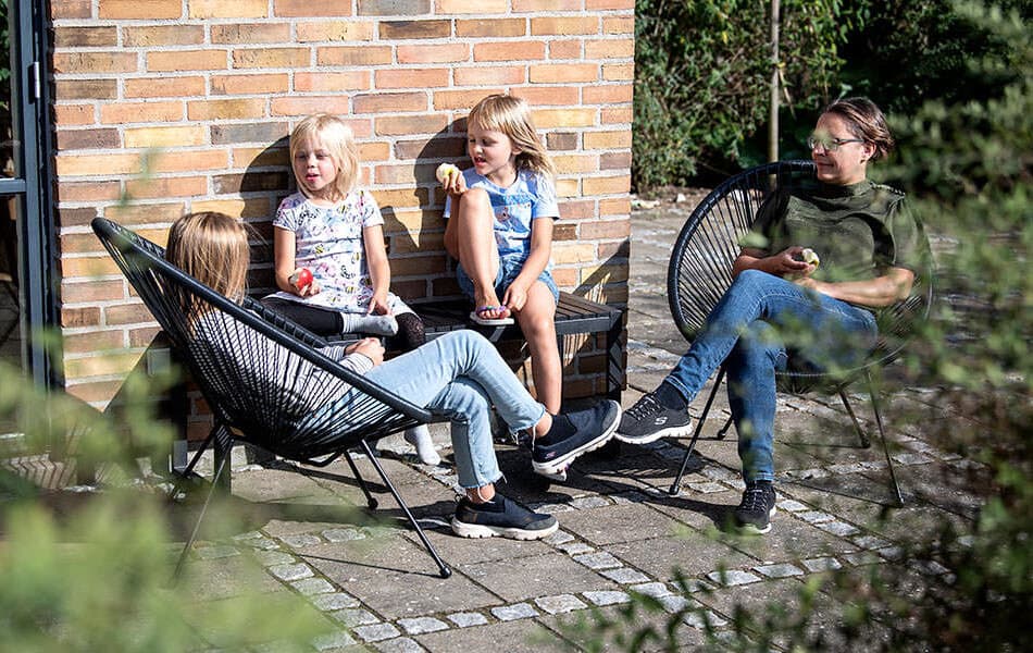 Familie sidder på lille terrasse ved bolig og nyder solen