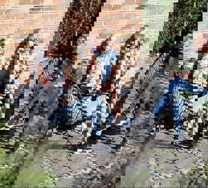 Familie sidder på lille terrasse ved bolig og nyder solen