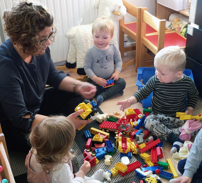 Dagplejer sidder på gulvet og leger med fire børn