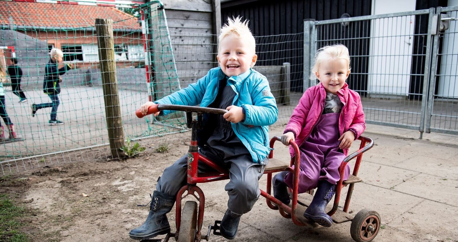 Dreng og en pige sidder på deres trehjulet cykler og er glade